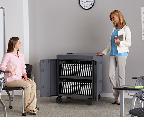 a Bretford CUBE Cart full of laptops in a room with two women