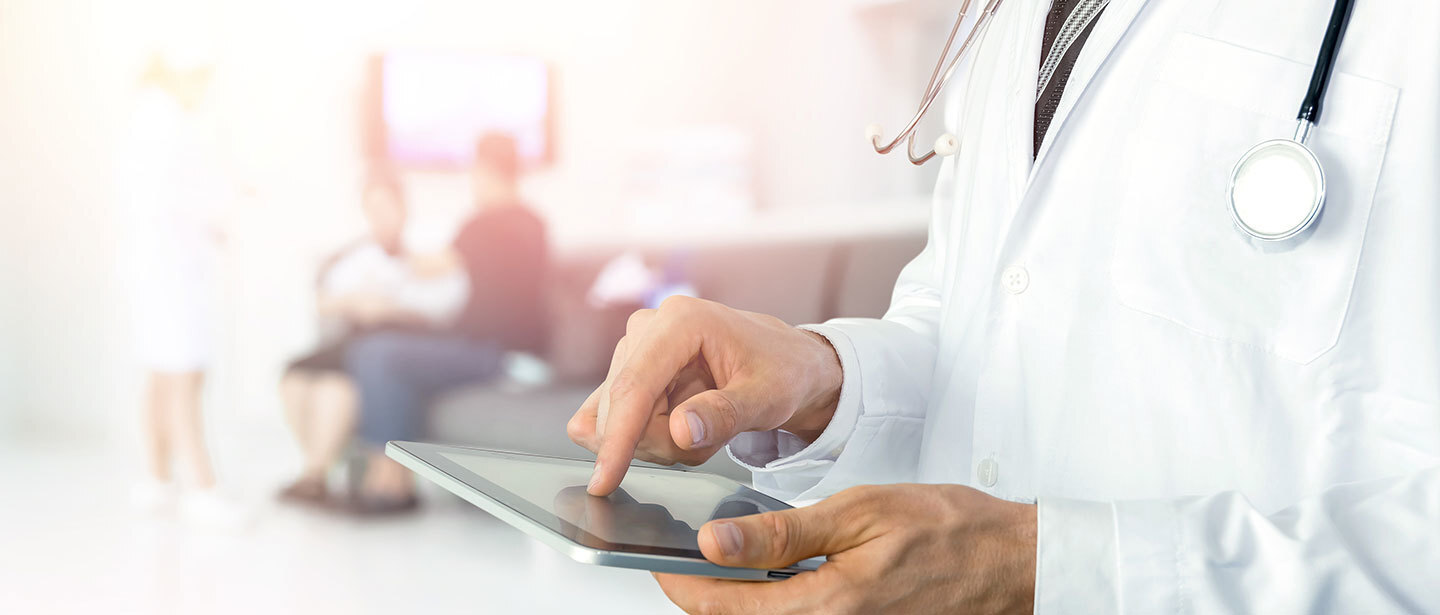 a doctor using a tablet, while some patients are sitting on a sofa at the back of the room