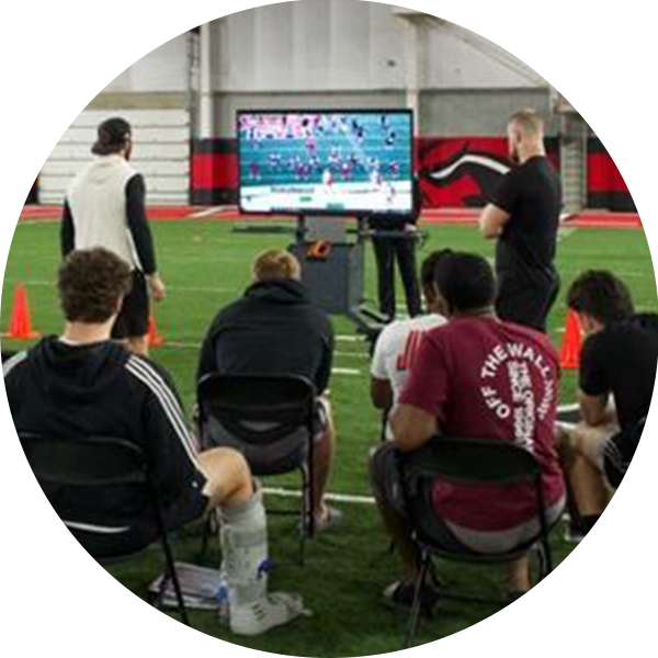 group of athletes with Jon Shalala, coach of Arkansas State watching a game on a Bretford Cordless Explorer Display Cart