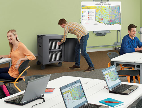 a man taking a chromebook from a Bretford CUBE Cart Mini in a classroom full of students