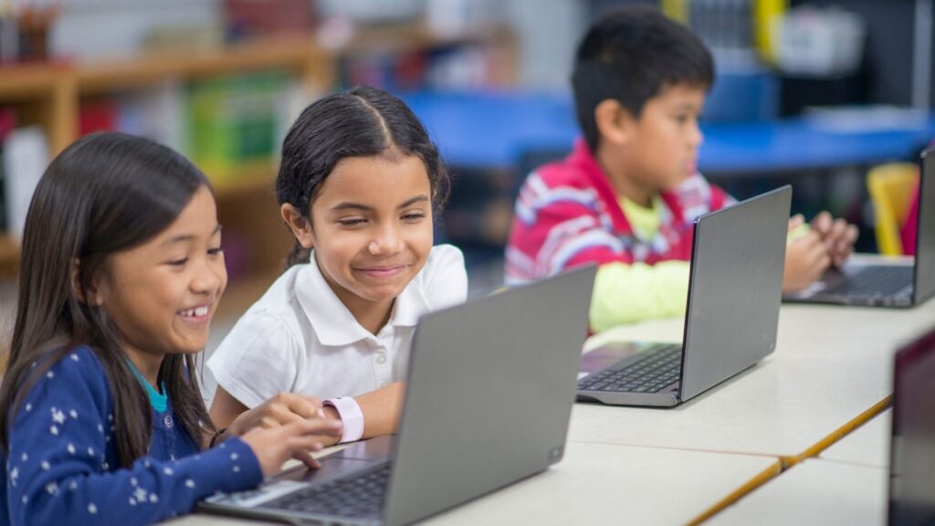 three children studying with their laptops on a table in a classroom