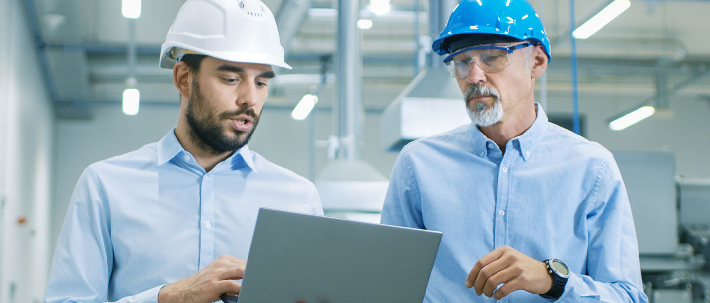 two men wearing helmets, reviewing some information on a laptop together