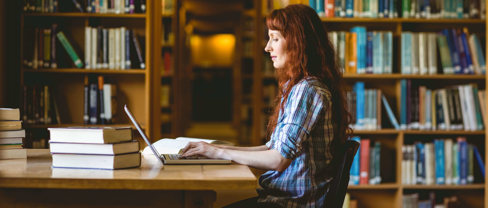 a woman in a library studying at a table using a laptop computer